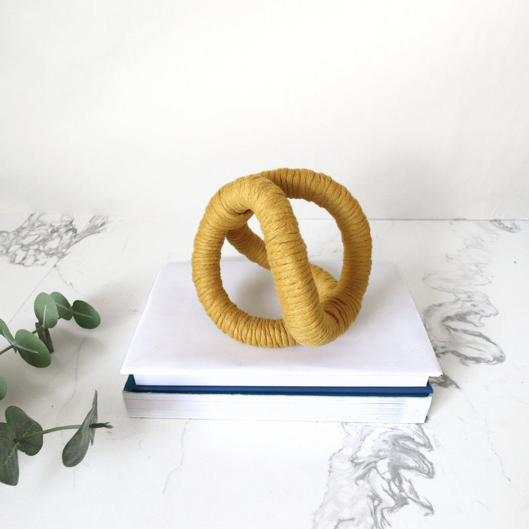 In situ display of infinity knot decor in mustard color used on table with stack of books adding texture and dimensions to the study room.