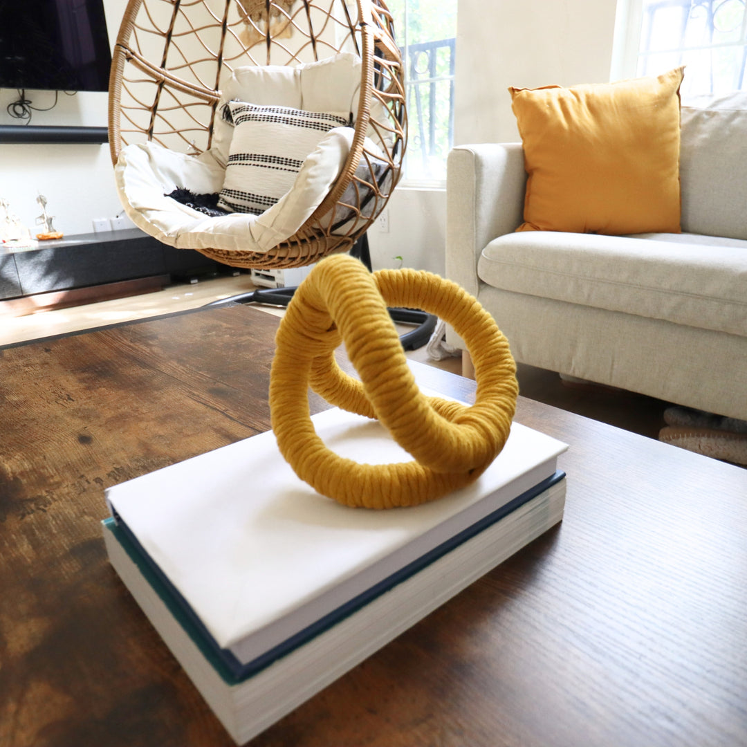 Display of knotted rope sculpture in mustard /yellow on a coffee table in a modern living room, adding texture and artisan flair to the conversational area.