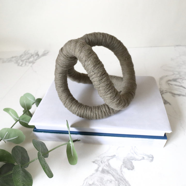 Console table decor in sage showcasing infinity knot made with one continuous jute rope and wrapped with cotton. Perfect rope sculpture for gift for new homeowners, wedding gift, mothers day gift.