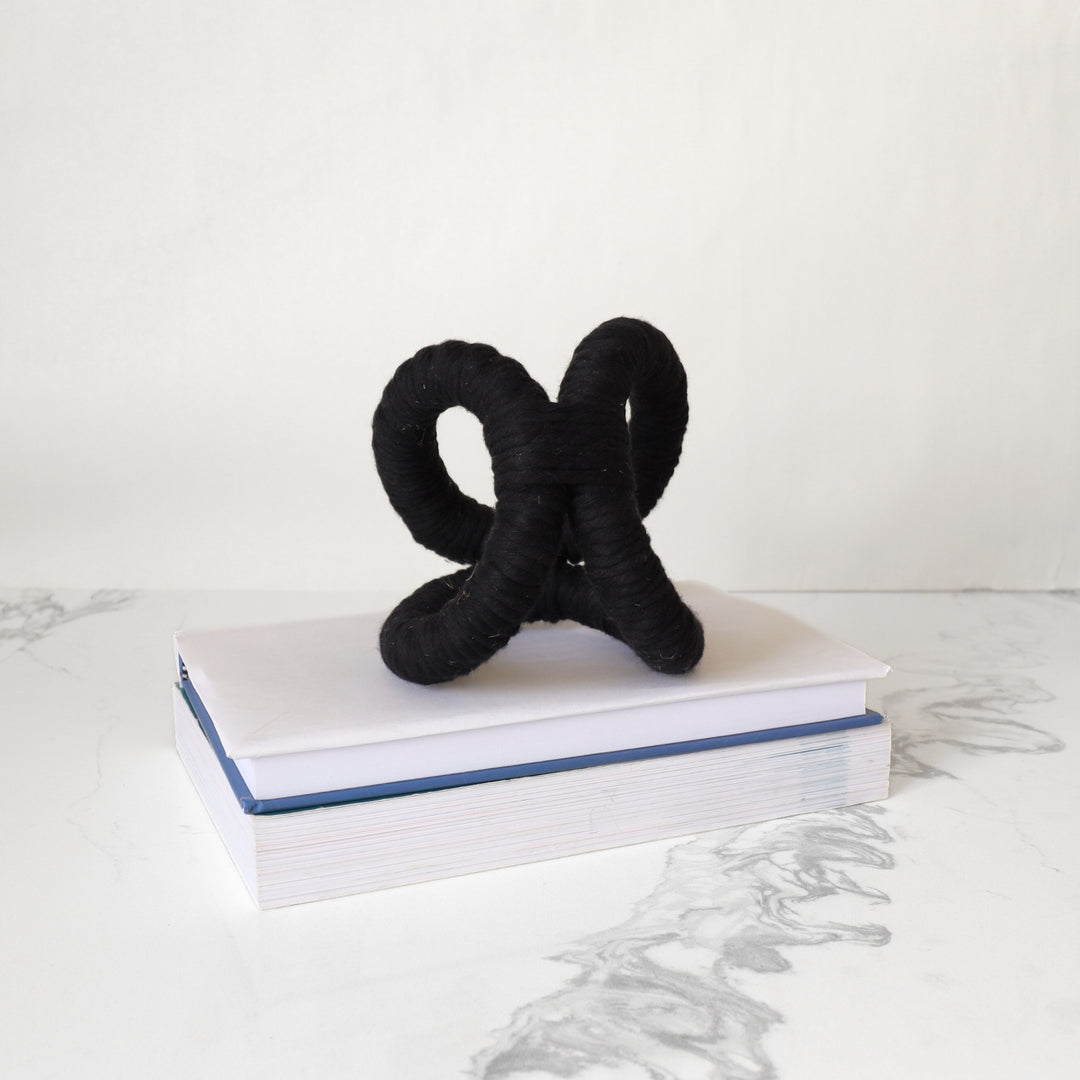In situ display of infinity knot decor in black color used on table with stack of books  adding texture and dimensions to the study room. 