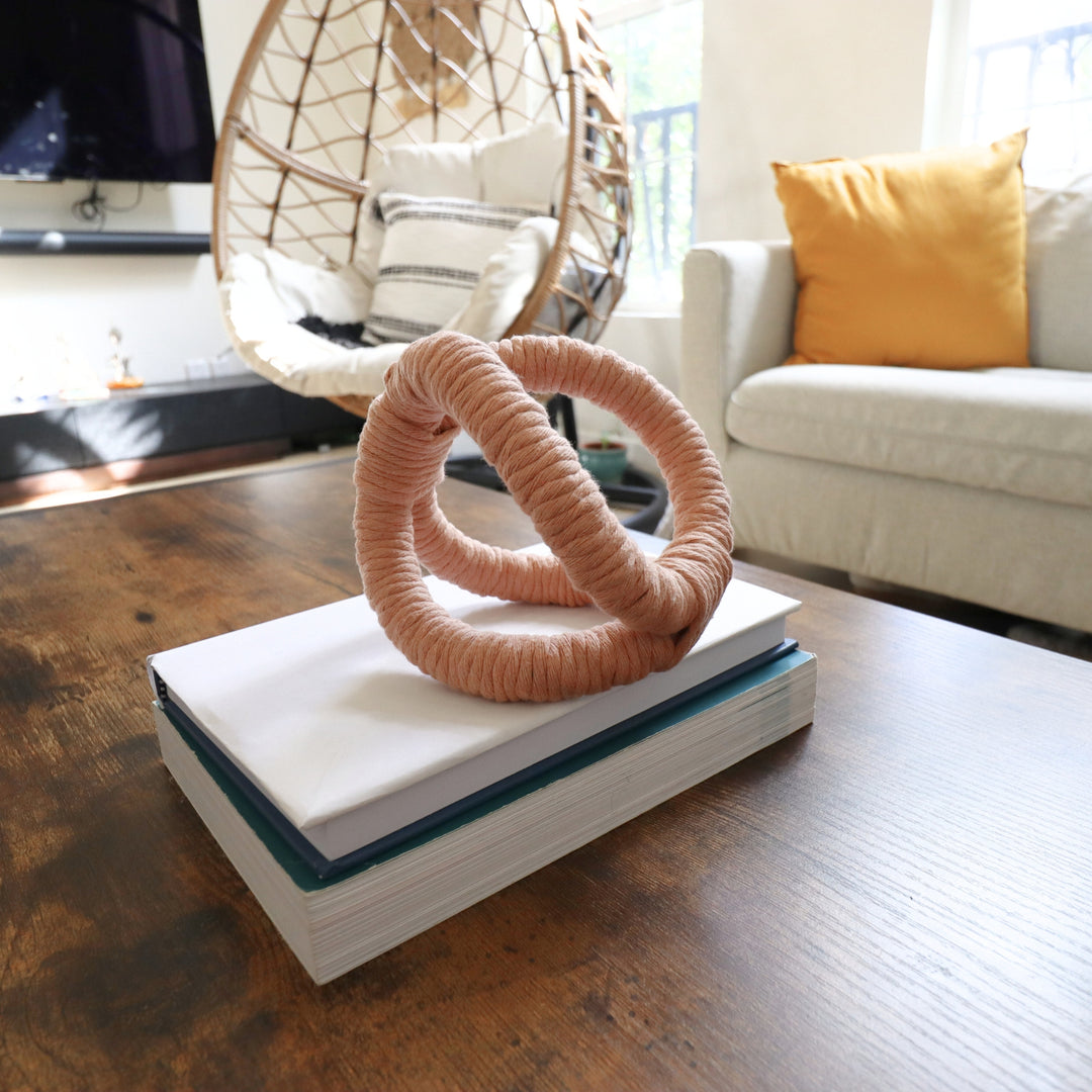 Display of knotted rope sculpture in peach fuzz/ pink color on a coffee table in a modern living room, adding texture and artisan flair to the conversational area.