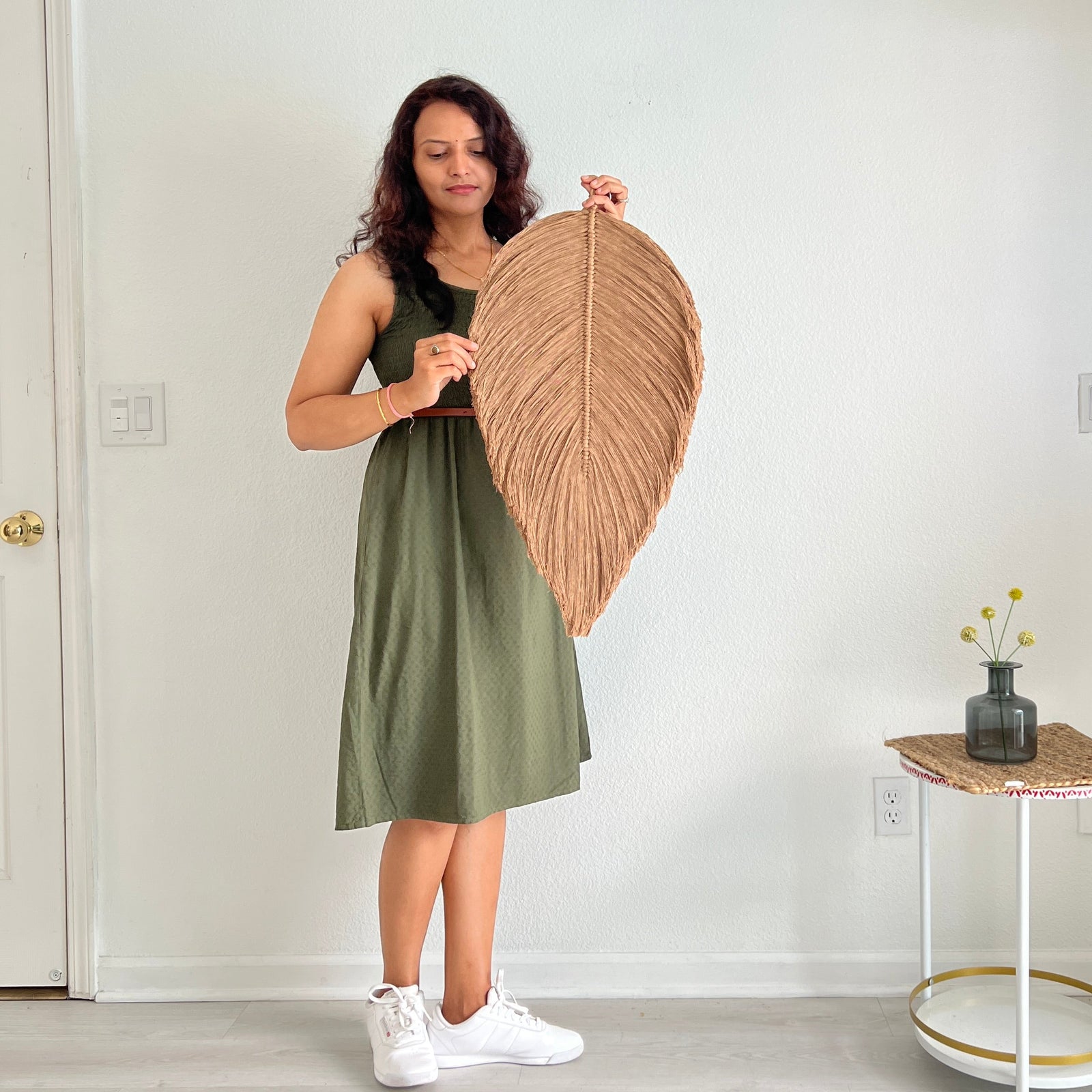 Woman holding a large woven leaf-shaped decor item in a minimalistic room.