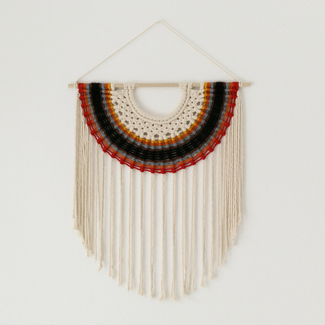 Woven wall hanging with concentric circles of red, orange, and black on a white background