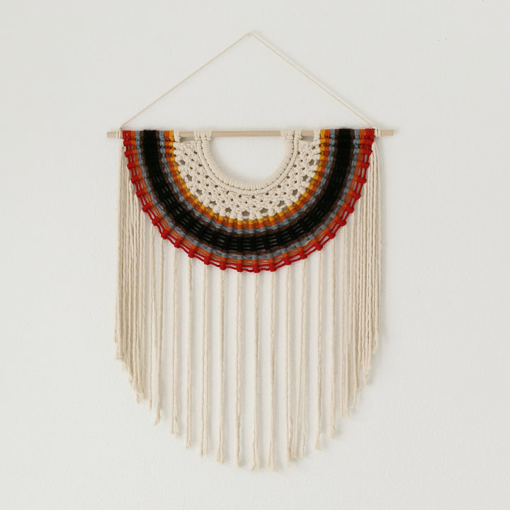 Woven wall hanging with concentric circles of red, orange, and black on a white background