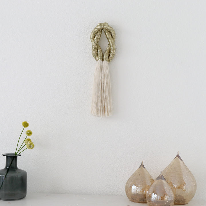 Gold knot made from jute and cotton sculpture placed on a white mantel, adding texture and warmth to the decor.