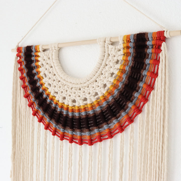 Colorful macrame wall hanging with concentric circles on a white background