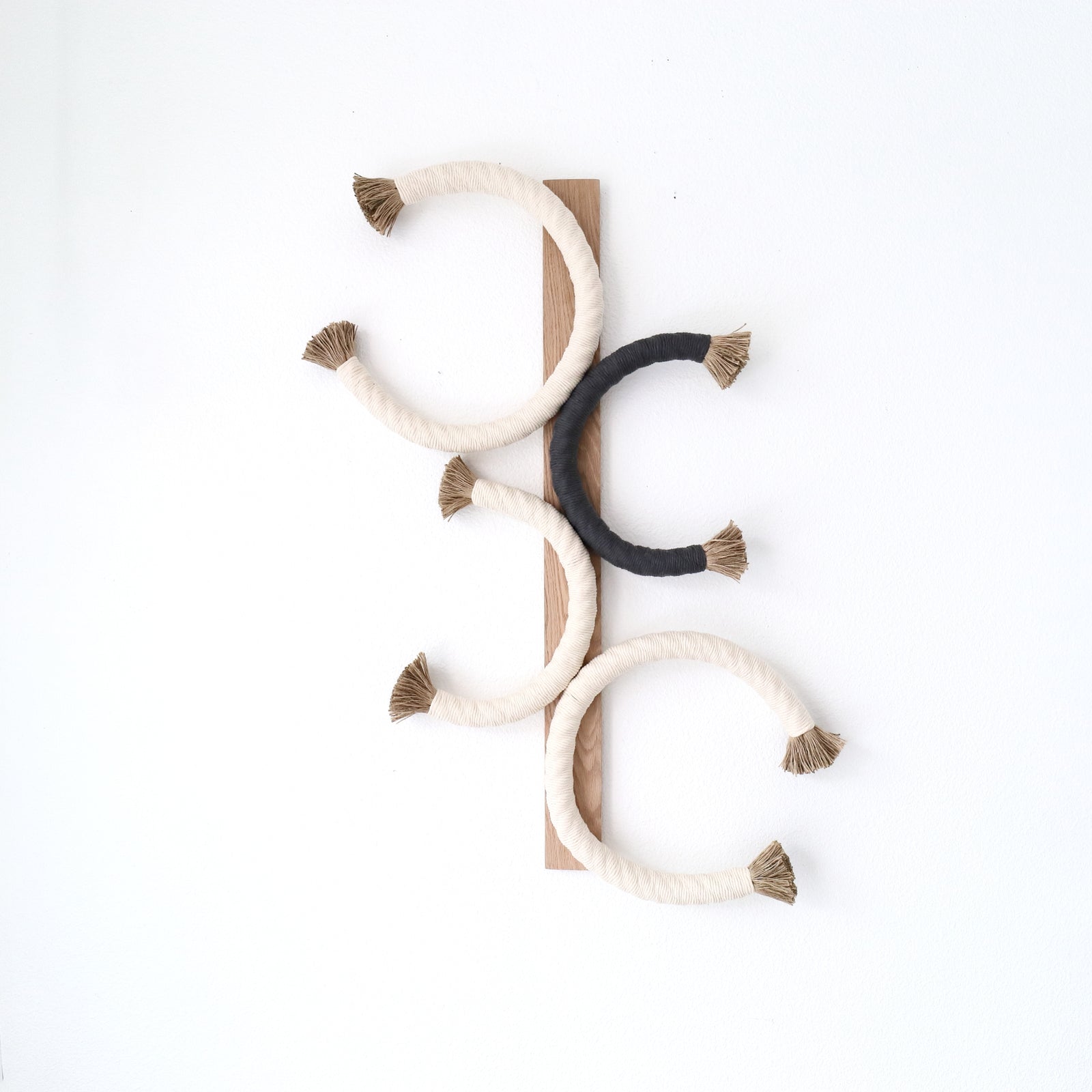 Artistic rope sculpture featuring interlaced circles with contrasting tassel accents, mounted on wood for a minimalist aesthetic, Unique Fiber Art, Earthy Tones, Jute Artworks - Coastal Farm House, Cottage Style, Eco-friendly living, Neutral Decor, Contemporary fiber art wall sculpture 