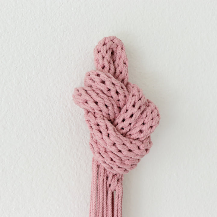 Close up view of pink knotted sculpture showcasing intricate knotwork and modern design on white wall.