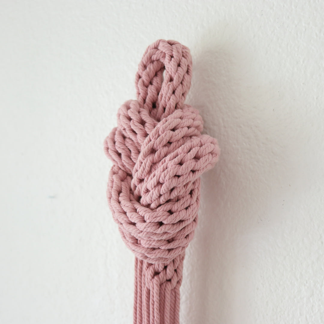 Side view of pink knot sculpture for wall, displayed in a tall space, adding a pop of color and artistic dimension.